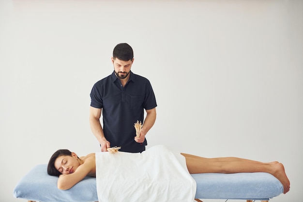 Guy usa bastoncini speciali La giovane donna è sdraiata quando l'uomo fa il massaggio del suo corpo alla spa