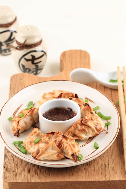 Gyoza Asian Potstickers con salse servite in ceramica marrone piatto in stile giapponese con bacchette e cipollotto su sfondo di legno bianco. Airfryer Cottura senza olio.