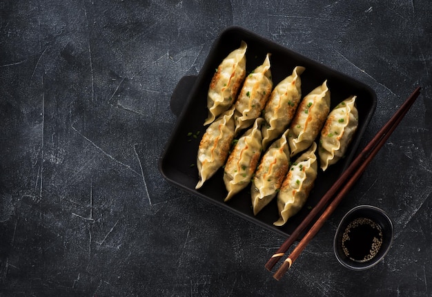 Gyoza fritti in padella su uno sfondo di cemento nero e spazio per la copia del testo, vista dall'alto