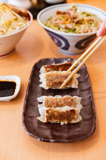 Gyoza (gnocchi giapponesi in padella) tenuti da bacchette servite con salsa e olio di sesamo.