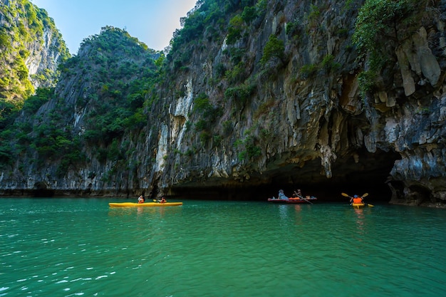 Ha Long VIETNAM MAR 12 2023 Giunche turistiche che galleggiano tra rocce calcaree a Ha Long Bay persone che fanno kayak all'interno di una grotta nella baia di Lan Ha vicino alla baia di Halong Vietnam
