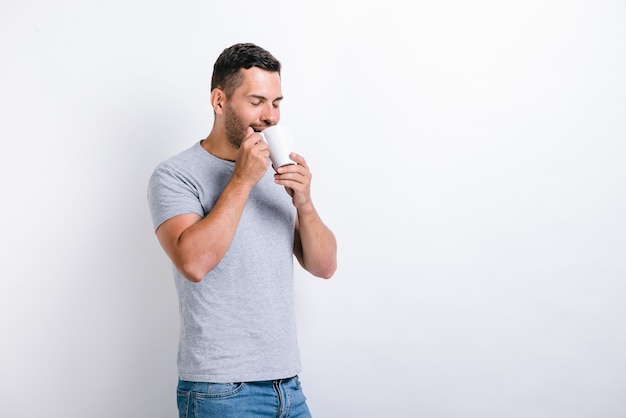 Ha un ottimo profumo. Mezzo busto vista verticale dell'uomo bello in piedi e annusando l'aroma del caffè dalla tazza. Concetto di bevande mattutine. Foto d'archivio