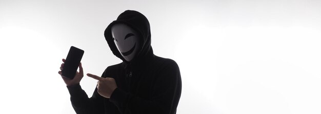 Hacker Anonymous e maschera facciale con smartphone in mano