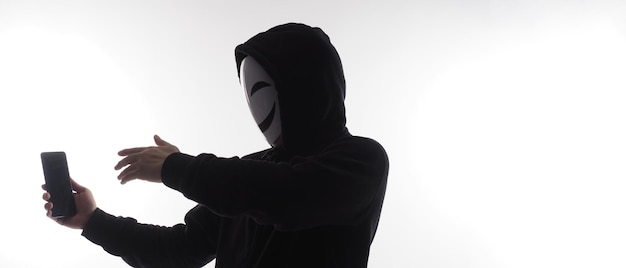 Hacker Anonymous e maschera facciale con smartphone in mano