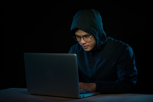 Hacker asiatico che hackera la rete di computer con il computer portatile al buio. Concetto di sicurezza informatica