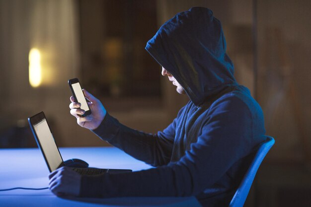 hacker con laptop e smartphone in una stanza buia