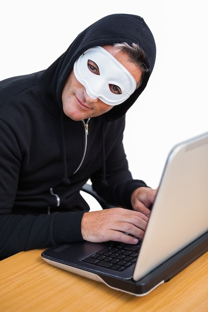 Hacker con maschera bianca utilizzando il computer portatile e guardando la fotocamera