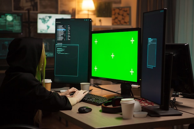 Hacker femminile che indossa una felpa con cappuccio davanti al computer con schermo verde.