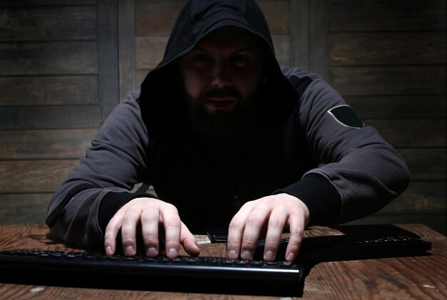 Hacker nel cappuccio nero in una stanza con pareti di legno