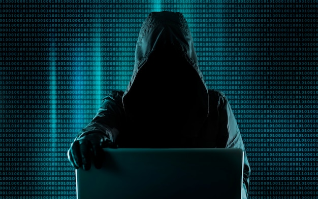 hacking system, cybercriminal behind a laptop, digital binary code in the background. hacker breaks into the system