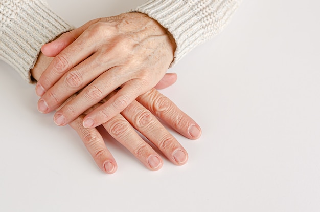 Hahds di una donna anziana sul muro bianco. Primo piano, copia spazio.