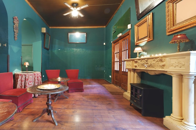 Hall di un bar in stile vintage con pareti verdi un camino in marmo e poltrone rivestite in tessuto rosso tavoli rotondi in legno e un ventilatore con pale sul soffitto
