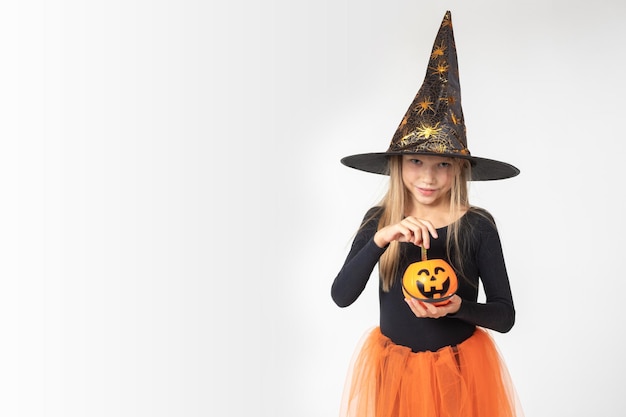 Halloween per bambini Una bella ragazza carina con un costume da strega che indossa un cappello tira fuori le caramelle da un cesto a forma di lanterna di Jack