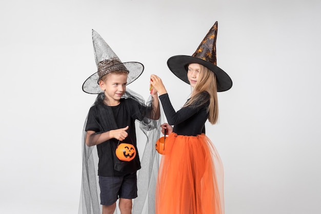 Halloween per bambini Una bella ragazza carina con un costume da strega e un ragazzo con un costume da mago tirano fuori le caramelle da un cestino