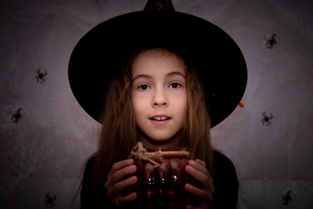 Halloween per bambini Una ragazza sorridente con un cappello da strega con bu palla arancione si prepara a festeggiare.