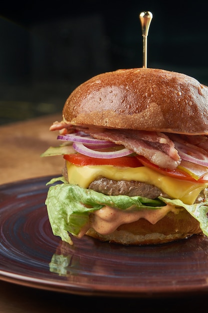 Hamburger appetitoso con manzo, pomodoro, cipolla, lattuga, pancetta e formaggio fuso in un piatto di ceramica scura