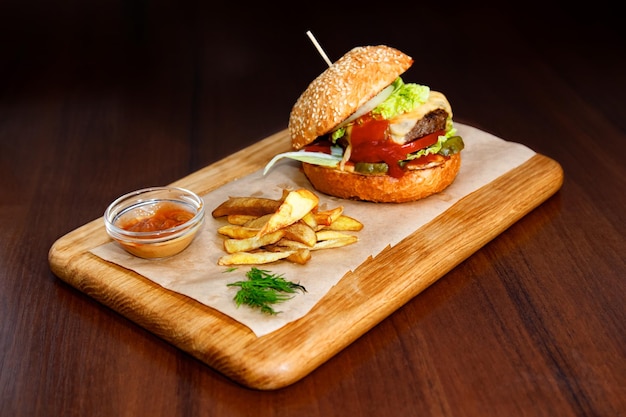 Hamburger appetitoso con patatine fritte e salsa su una lavagna con uno sfondo scuro