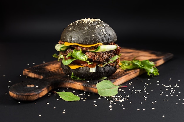 Hamburger artigianale gustoso con panino nero su sfondo nero
