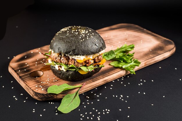 Hamburger artigianale gustoso con panino nero su sfondo nero