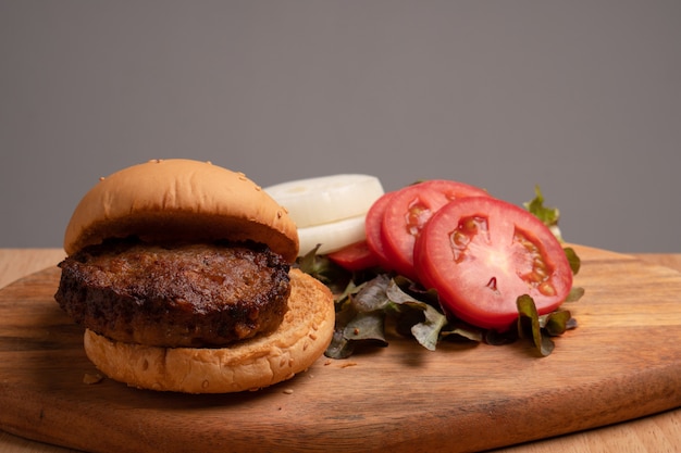 Hamburger casalingo saporito fresco con gli ortaggi freschi, lattuga, pomodoro, formaggio accanto ai pomodori affettati su un tagliere.