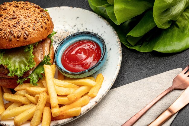 Hamburger con bistecca di lattuga e formaggio servito con patatine fritte e salsa su fondo scuro