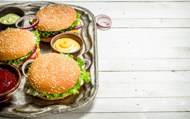 Hamburger con carne di manzo e verdure su un vassoio in acciaio su un fondo di legno bianco