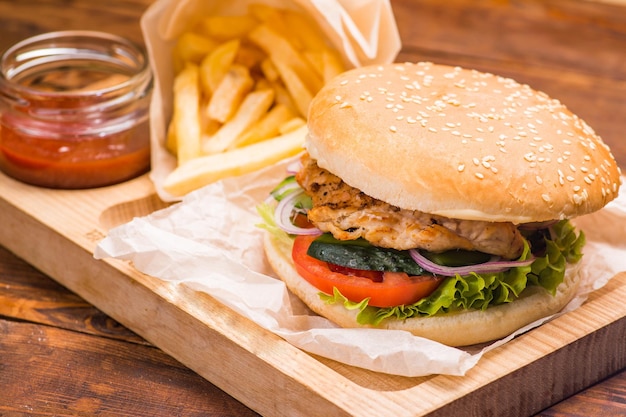 Hamburger con cotoletta in un panino bianco sullo sfondo di patatine fritte e salsa di pomodoro