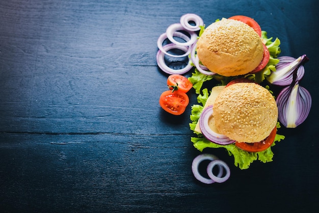 Hamburger con formaggio, carne, pomodori, cipolle ed erbe aromatiche su fondo in legno Vista dall'alto Spazio libero