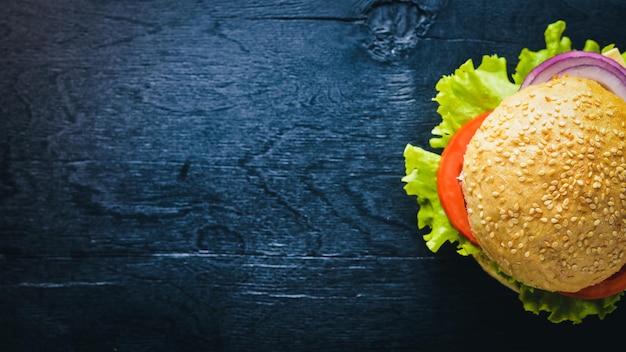 Hamburger con formaggio, carne, pomodori, cipolle ed erbe aromatiche su fondo in legno Vista dall'alto Spazio libero