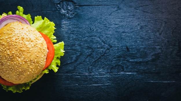 Hamburger con formaggio, carne, pomodori, cipolle ed erbe aromatiche su fondo in legno Vista dall'alto Spazio libero