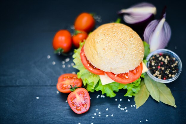 Hamburger con formaggio, carne, pomodori, cipolle ed erbe aromatiche su fondo in legno Vista dall'alto Spazio libero