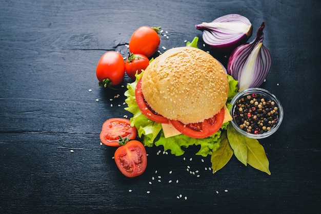 Hamburger con formaggio, carne, pomodori, cipolle ed erbe aromatiche su fondo in legno Vista dall'alto Spazio libero