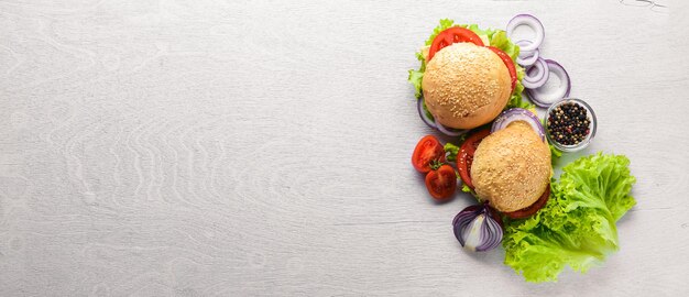 Hamburger con formaggio, carne, pomodori, cipolle ed erbe aromatiche su fondo in legno Vista dall'alto Spazio libero