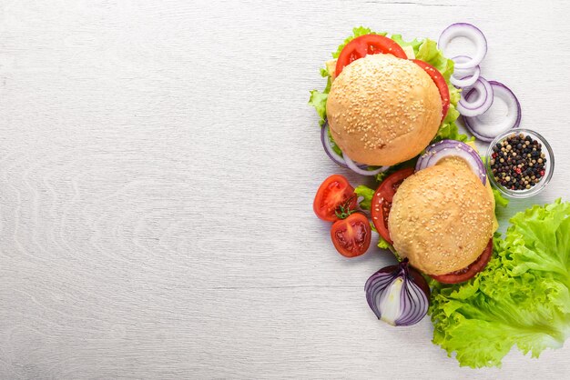 Hamburger con formaggio, carne, pomodori, cipolle ed erbe aromatiche su fondo in legno Vista dall'alto Spazio libero