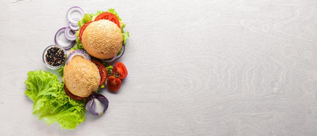 Hamburger con formaggio, carne, pomodori, cipolle ed erbe aromatiche su fondo in legno Vista dall'alto Spazio libero