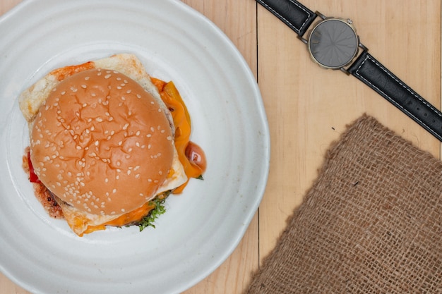 Hamburger con orologio da polso sul tavolo di legno.