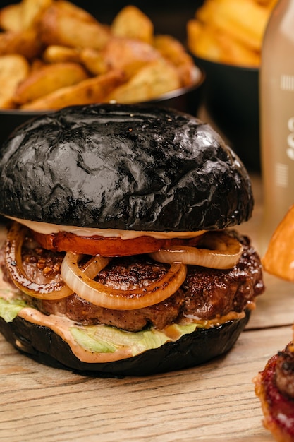 Hamburger con panino nero succoso tortino di cipolla anelli salsa di pomodoro su un tavolo di legno