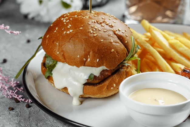 Hamburger con patatine fritte e salsa su un piatto bianco.