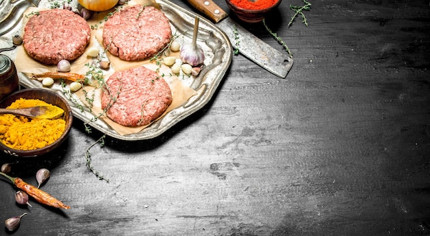 Hamburger crudo con aglio e spezie su un vassoio in acciaio. Sulla lavagna nera.