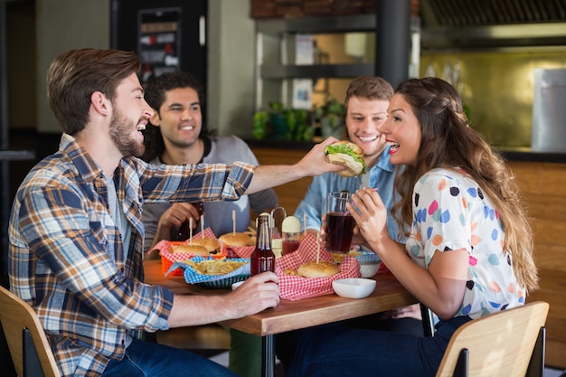 Hamburger d'alimentazione del giovane all'amico in ristorante