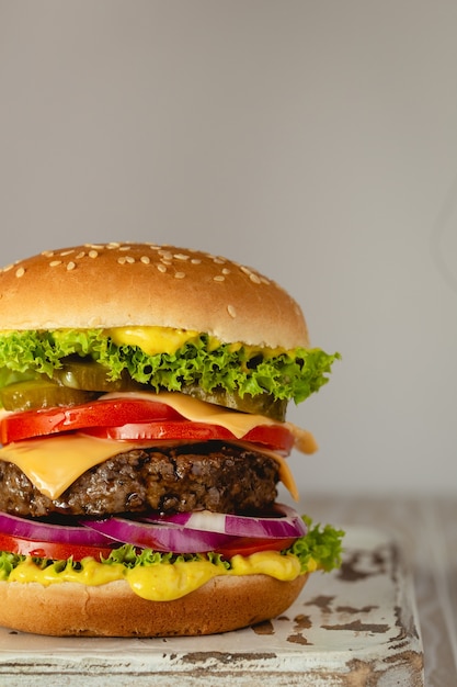 Hamburger delizioso con carne, formaggio fuso, salsa gocciolante e verdure su fondo rustico bianco. Hamburger gustoso appena fatto, primo piano