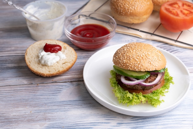 Hamburger delizioso su un piatto bianco su un legno e salse