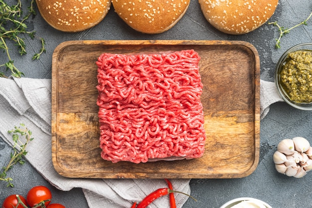 Hamburger di bistecca di manzo tritato crudo fresco con set di ingredienti di spezie, su vassoio di legno, su pietra grigia