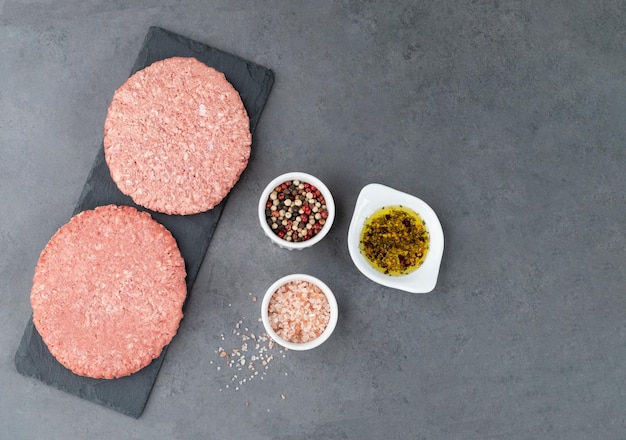 Hamburger di carne cruda su sfondo di pietra con condimenti e copia spazio