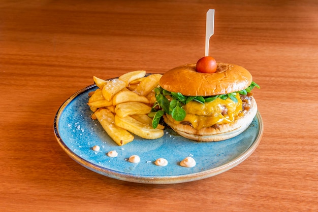 Hamburger di due carni con formaggio cheddar fuso, cipolla caramellata, germogli di valeriana, pomodorini allo spiedo e patatine fritte