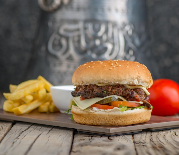 Hamburger di manzo croccante piccante con patatine fritte servite nella vista laterale del piatto su uno sfondo di tavolo in legno