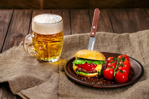 Hamburger di manzo fatto in casa e verdure fresche sul piatto di argilla con un bicchiere di birra sul tavolo di legno rustico.