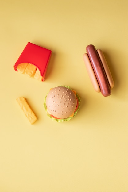 Hamburger di plastica, insalata, pomodoro, patate fritte con un hot dog su uno sfondo giallo