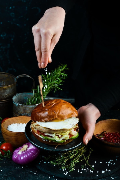 Hamburger di pollo fresco e gustoso su tavola di legno Nelle mani su sfondo nero
