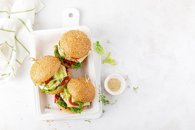Hamburger di pollo sandwich con hamburger di pollo formaggio pomodoro cetriolo lattuga fresca microgreen e ketchup su sfondo bianco Vista dall'alto